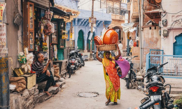 a woman in yellow saree carrying basket on her head